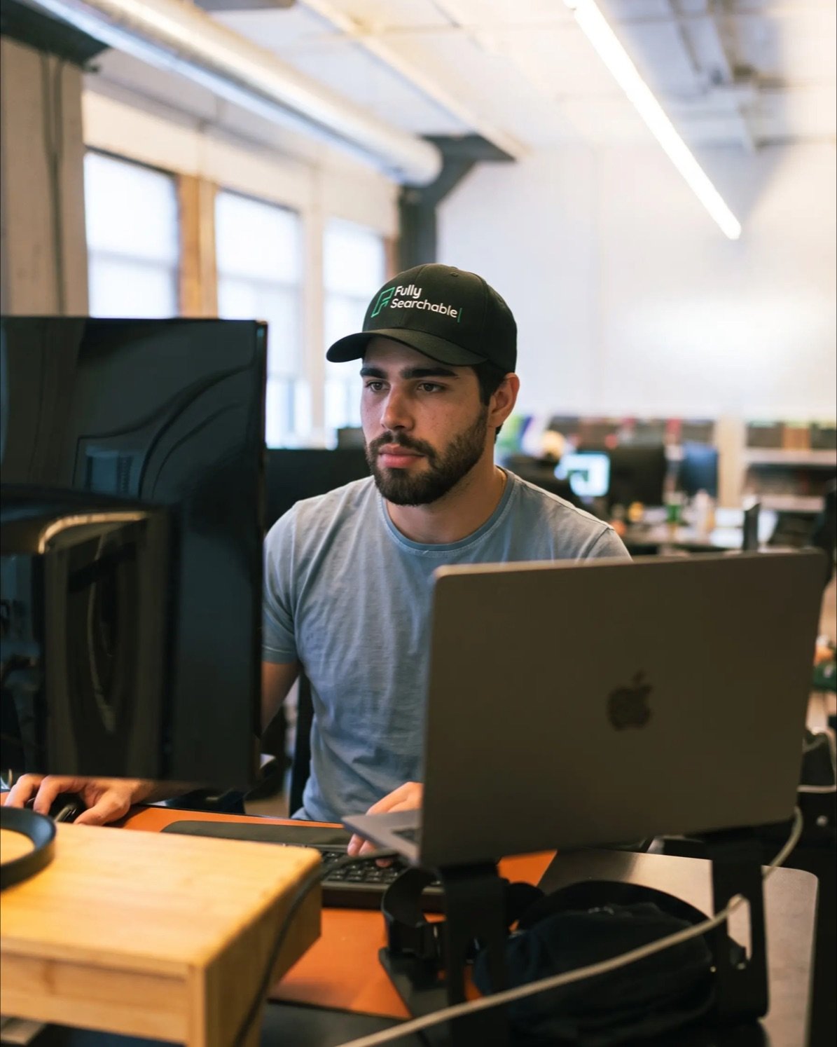 Fully Searchable team member wearing a branded cap, working at a standing desk in the office