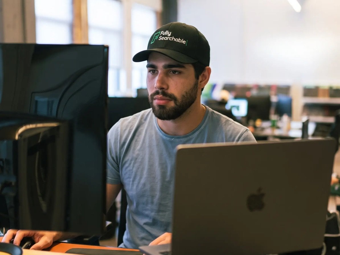 Fully Searchable team member wearing a branded cap, working at a standing desk in the office
